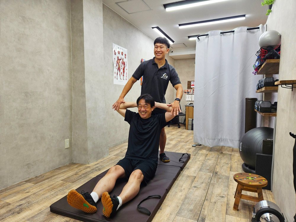 座った姿勢で上半身をひねる動きをトレーナーがサポート(イメージ)